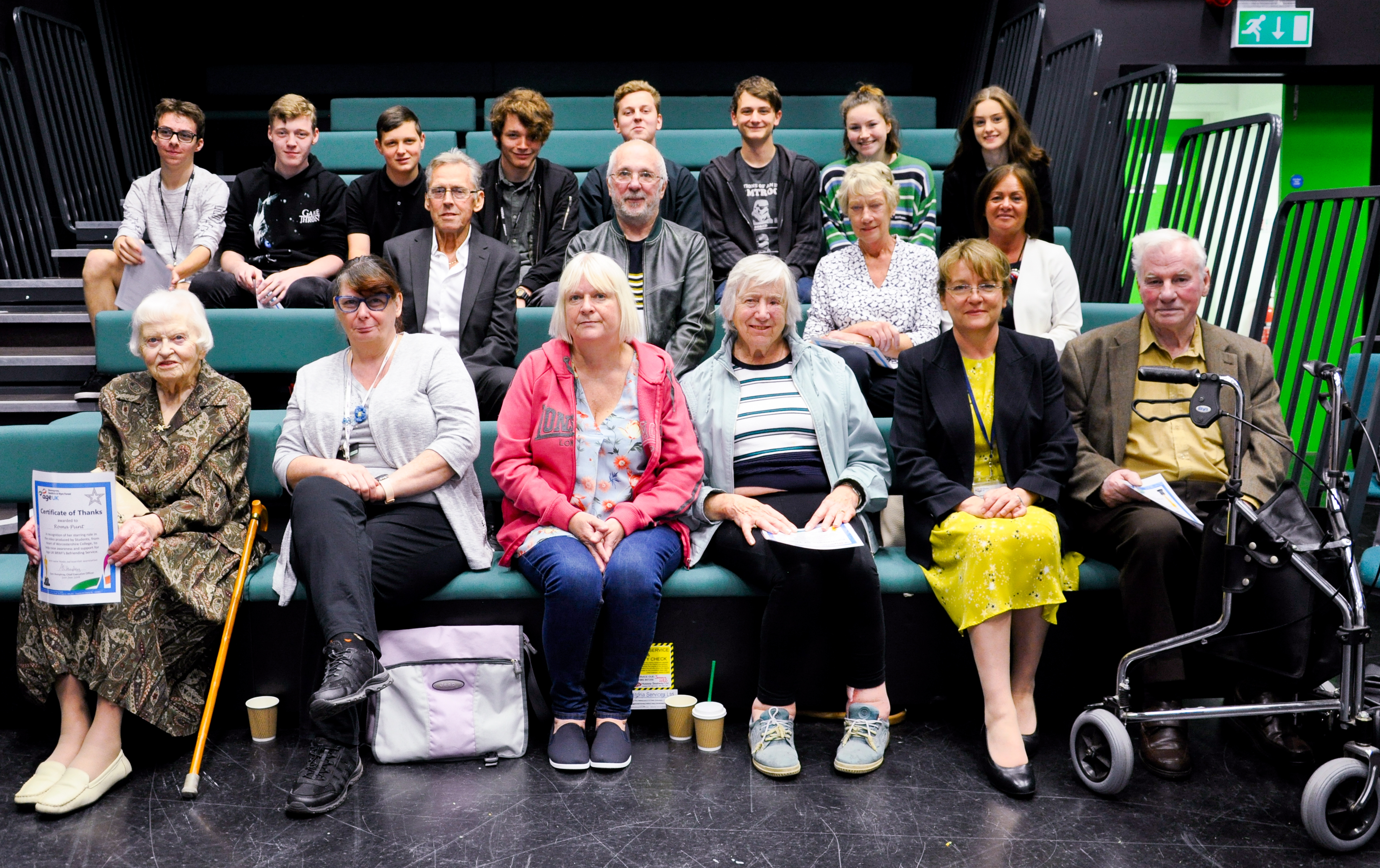 Group of senior adults and college students sat on green theatre benches in a black TV studio