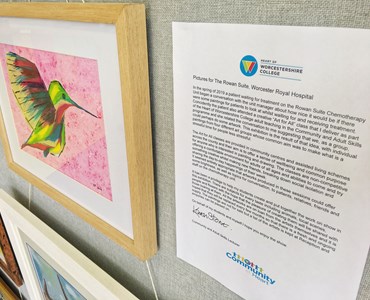 Grey wall holding a piece of artwork that depicts a humming bird in an oak frame. Letter pinned next to it that contains the HoW College logo.