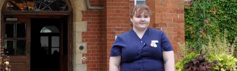 Female student in beauty therapy uniform stood outside large, country manor house