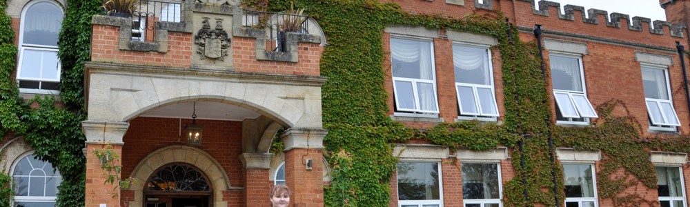 Female student in beauty therapy uniform stood outside large, country manor house