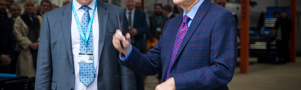 Two men in grey suits cutting blue ribbon at an opening ceremony