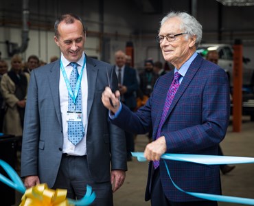 Two men in grey suits cutting blue ribbon at an opening ceremony