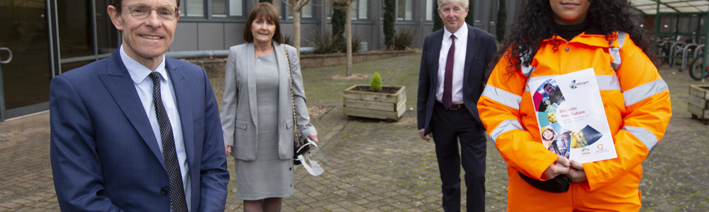 4 adults stood socially distanced outside the front of a College. 2 males wearing suits, one female wearing business attire and one female wearing orange high visibility jacket and trousers while holding a 'reignite your future' brochure.