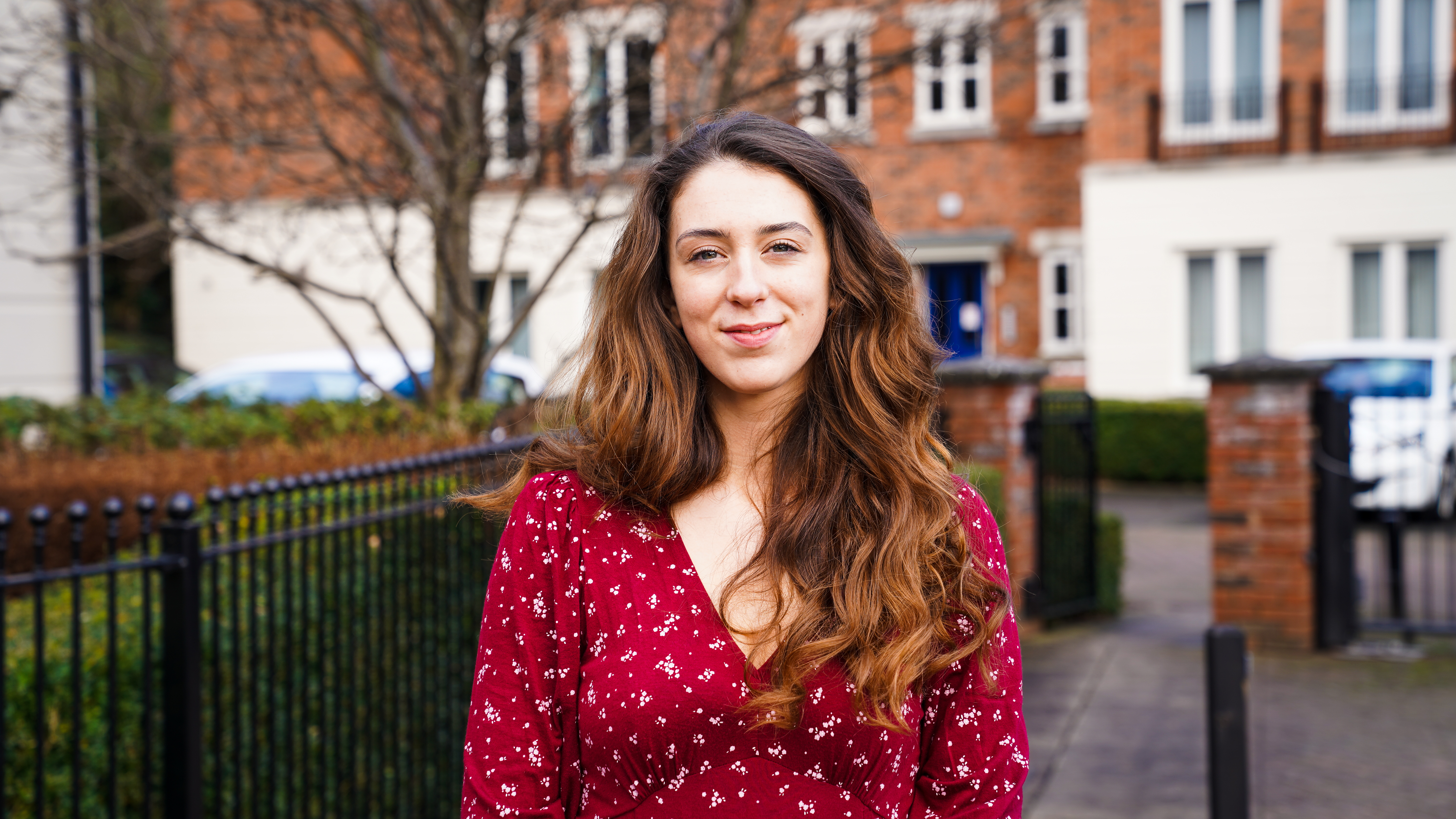 Image of a female stood outside near black railing, smiling at the camera