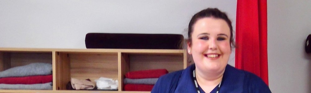 Female student in beauty therapy uniform smiling in front of beauty facilities.