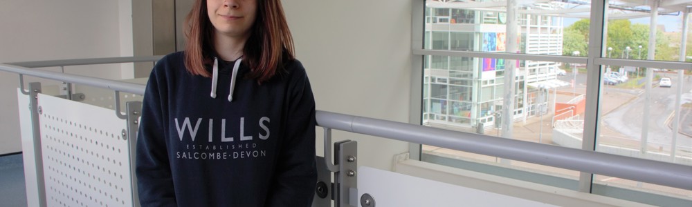 female student stood against a bannister smiling at the camera