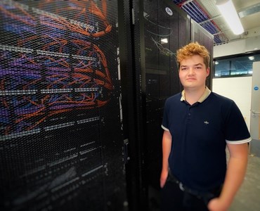 Male students stood against a computer server wall smiling at the camera