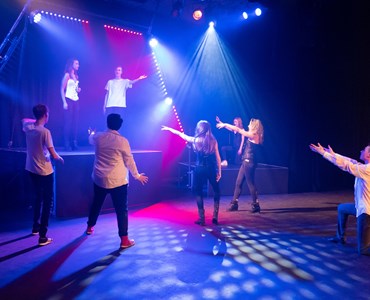 A group of students on stage in a dress rehearsal for performing arts