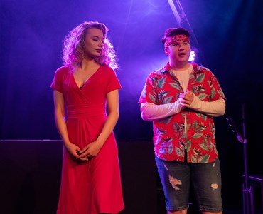 A performing arts dress rehearsal. a male and female student both dressed in red are stood next to each other