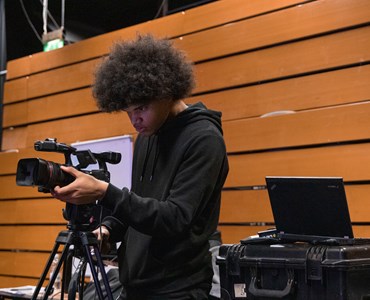 HoW College student dressed all in black, operates television camera, recording a performance