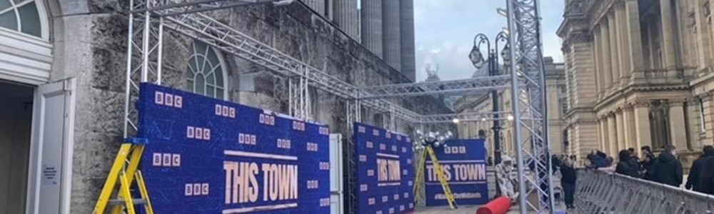 Picture of red carpet event being set up, with a backdrop that says this town