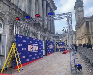 Picture of red carpet event being set up, with a backdrop that says this town